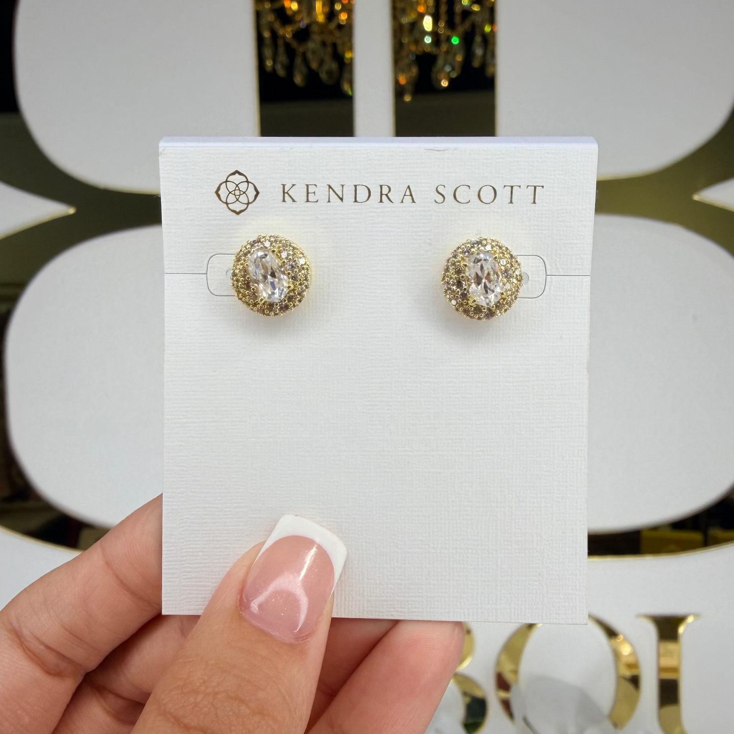 Kendra Scott earrings on a card held by a hand with a decorative background