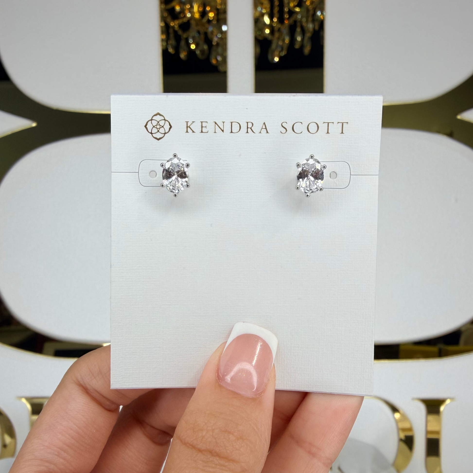 Kendra Scott earrings on a card held by a hand with a decorative background