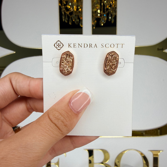 Kendra Scott earrings on a card held by a hand with a decorative background