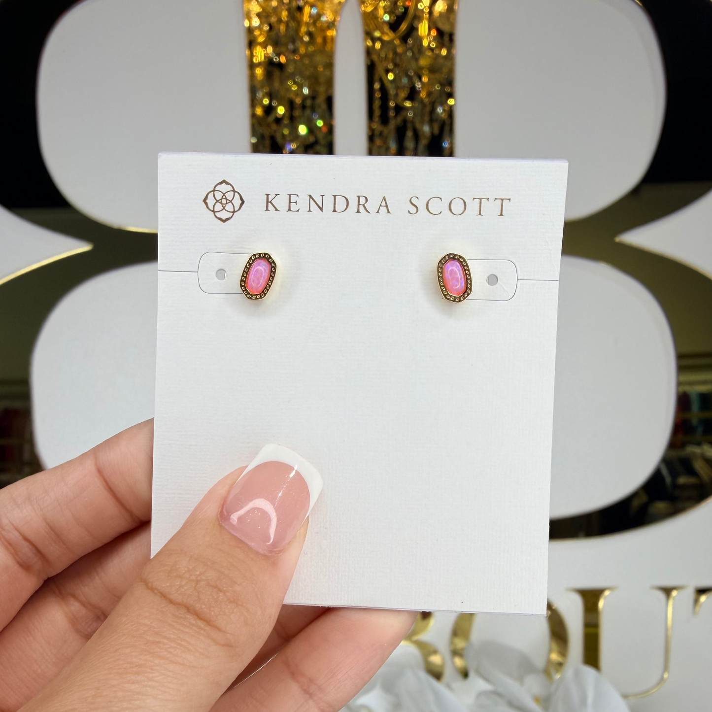Kendra Scott earrings on a card held by a hand with a decorative background