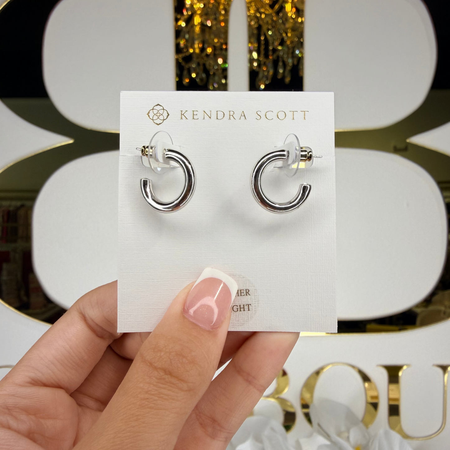 Kendra Scott earrings on a card held by a hand with a decorative background
