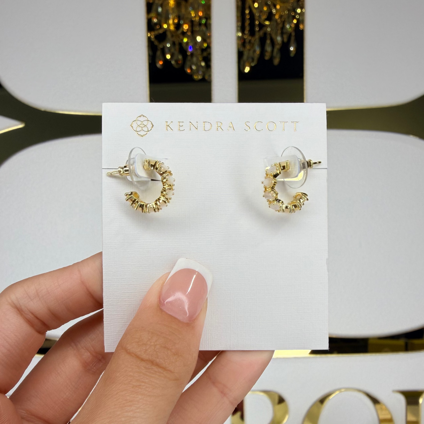 Gold hoop earrings on a Kendra Scott card held by a hand with a decorative background.