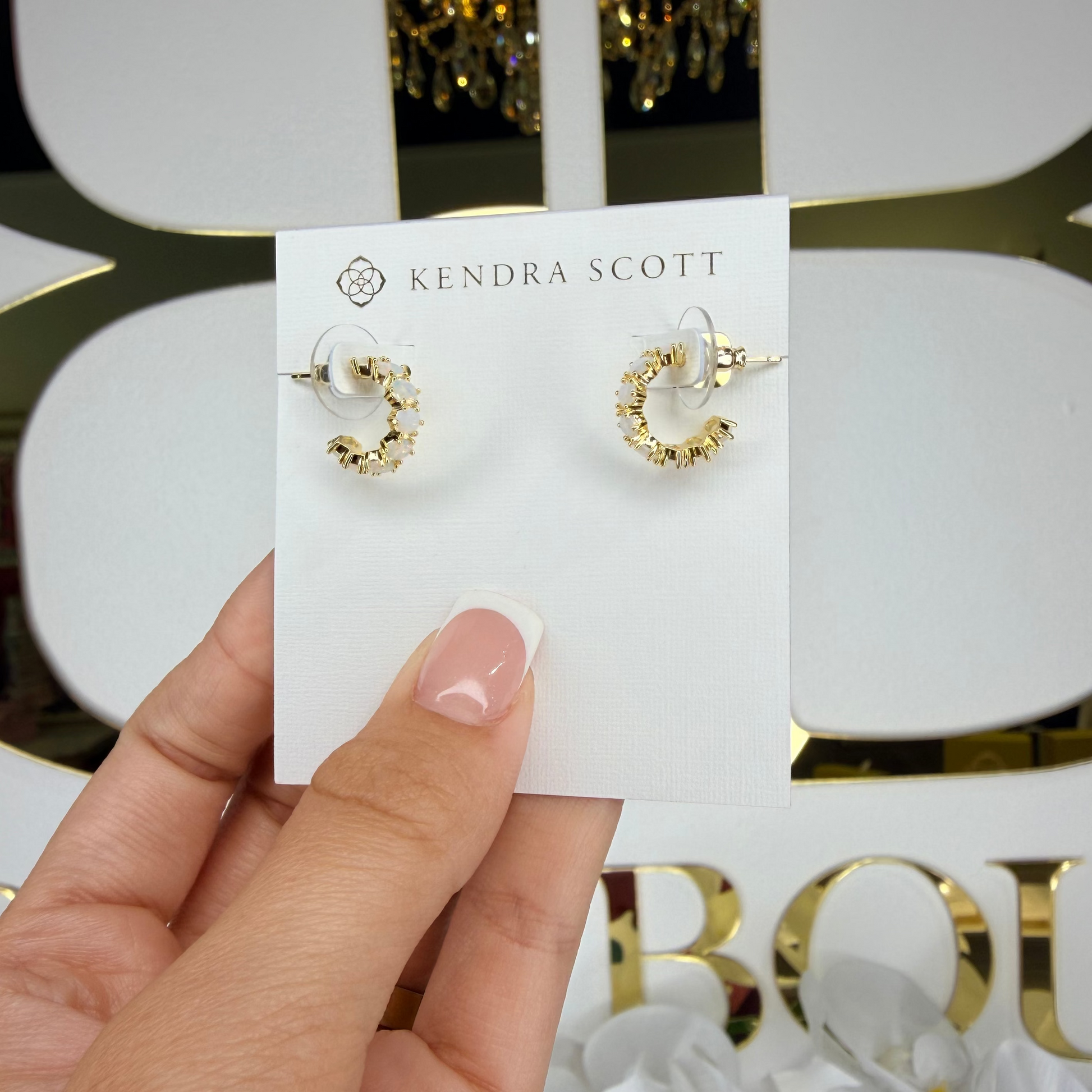 Gold hoop earrings on a Kendra Scott card held by a hand against a decorative background.