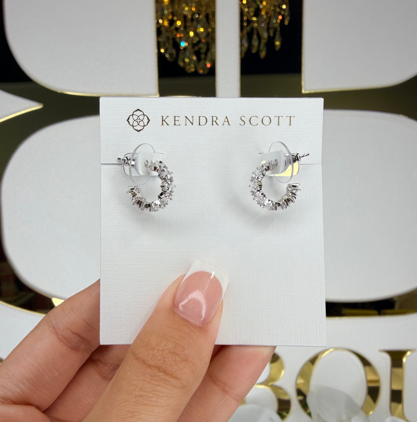 Kendra Scott earrings on a card held by a hand with a decorative background