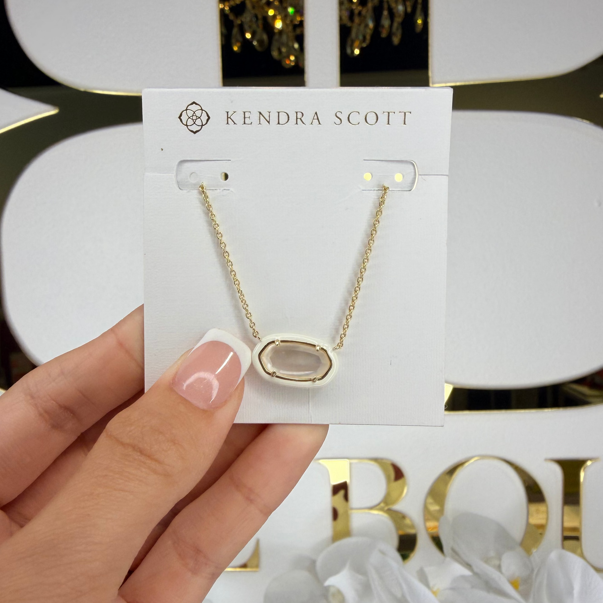 Kendra Scott necklace on a card held by a hand with a decorative background