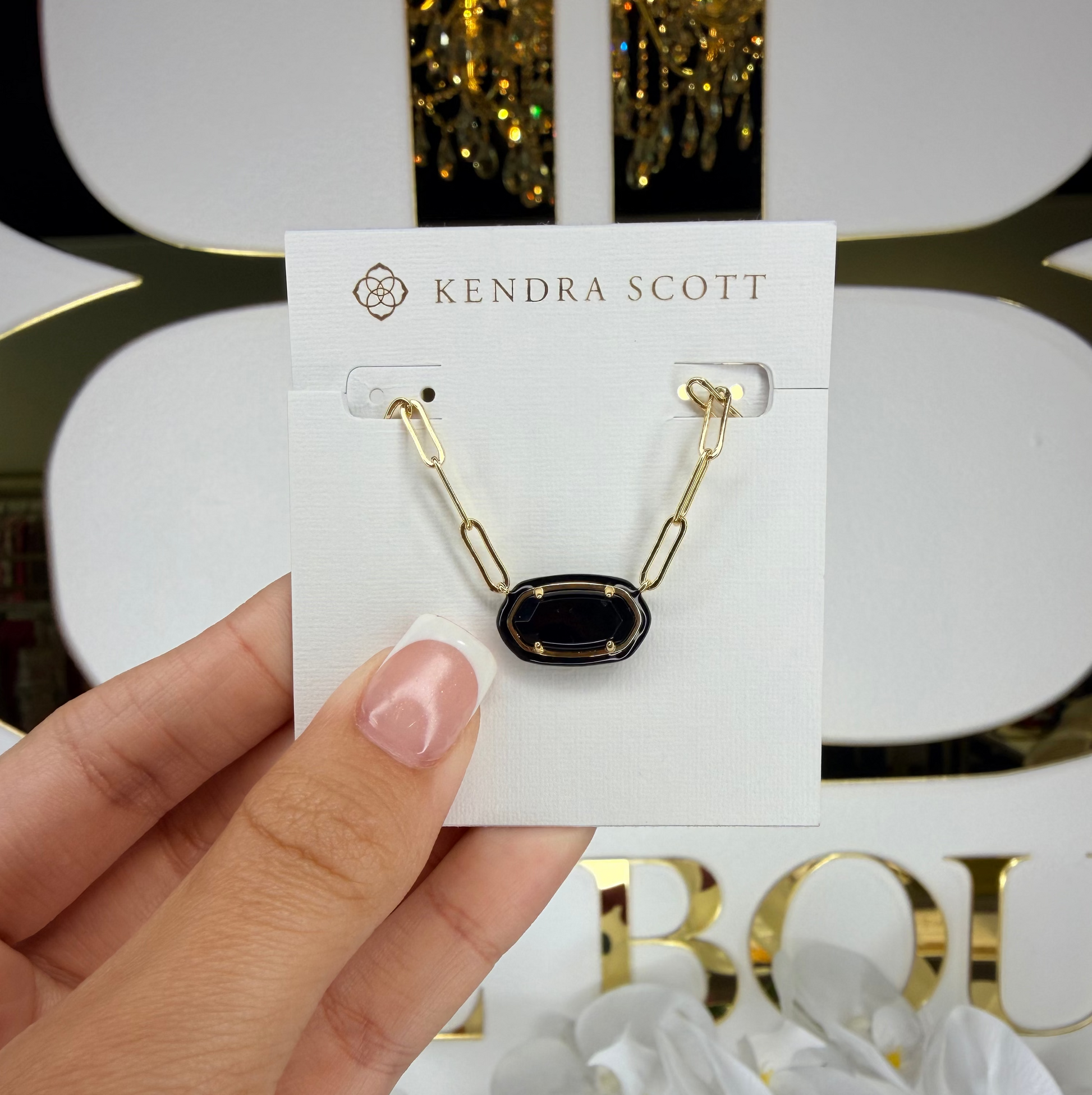 Kendra Scott necklace on a card held by a hand with a blurred background