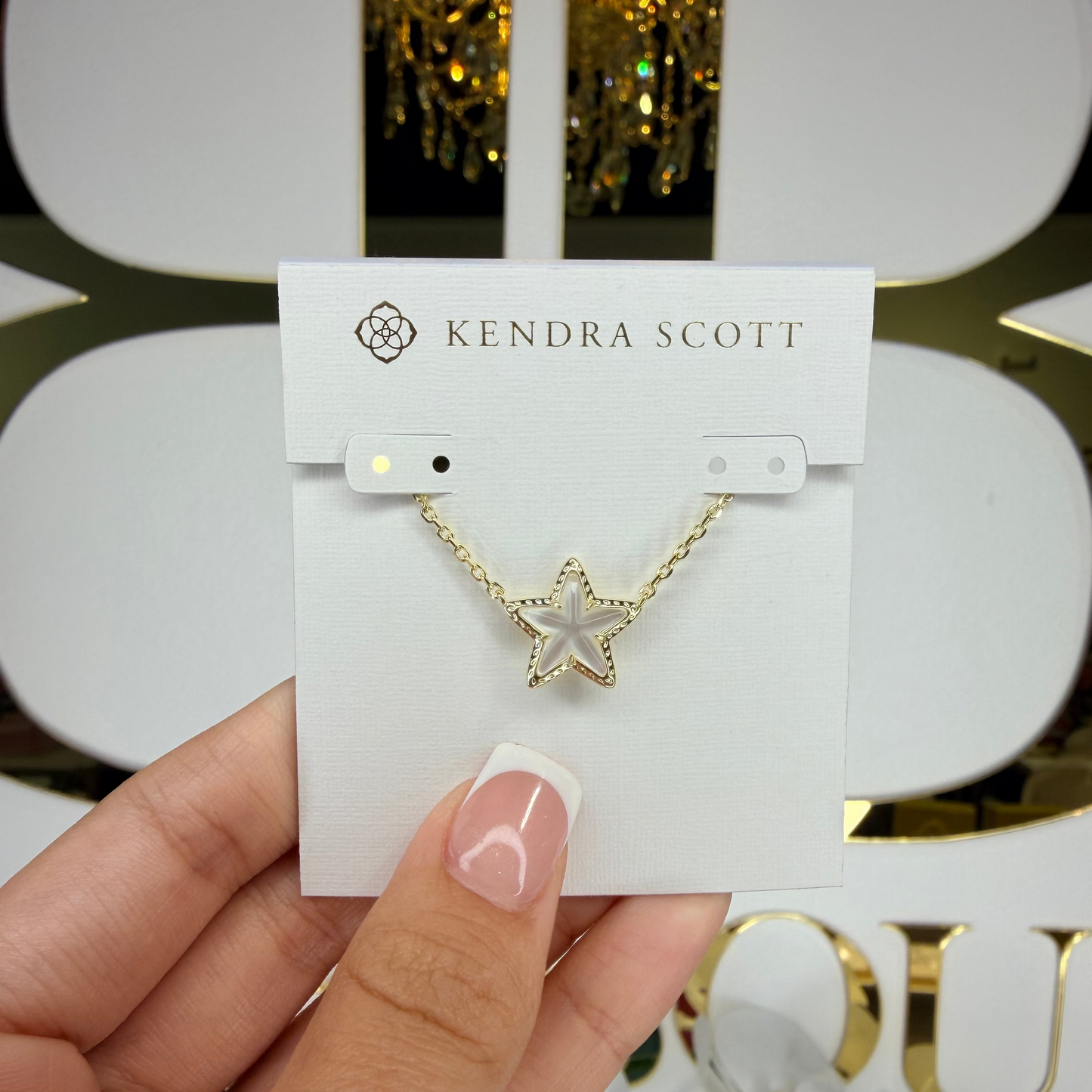 Star-shaped necklace on a Kendra Scott card held by a hand with a blurred background