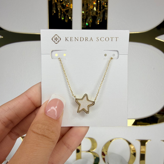 Gold star necklace on a Kendra Scott card held by a hand with a blurred background