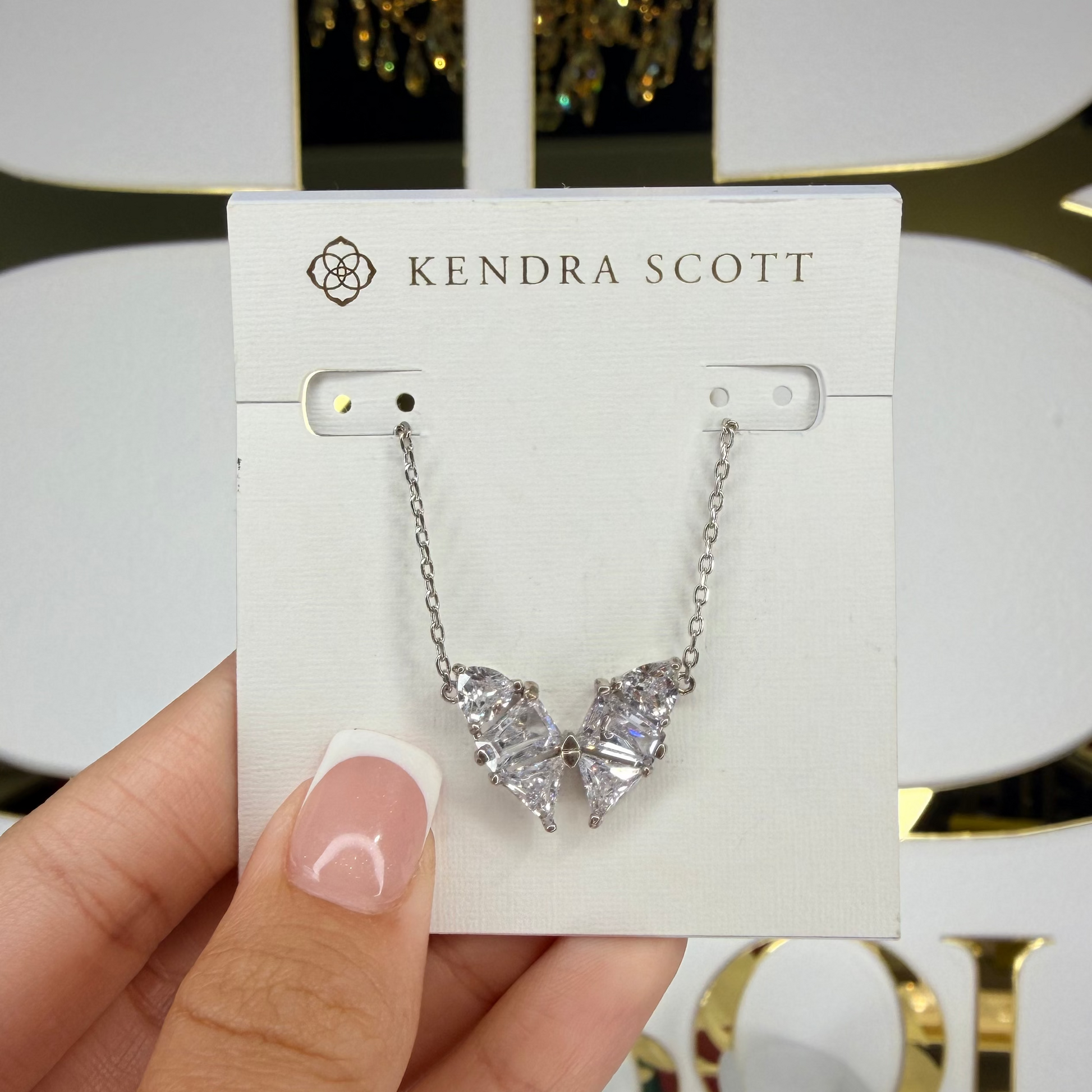Kendra Scott earring on a card held by a hand with a decorative background