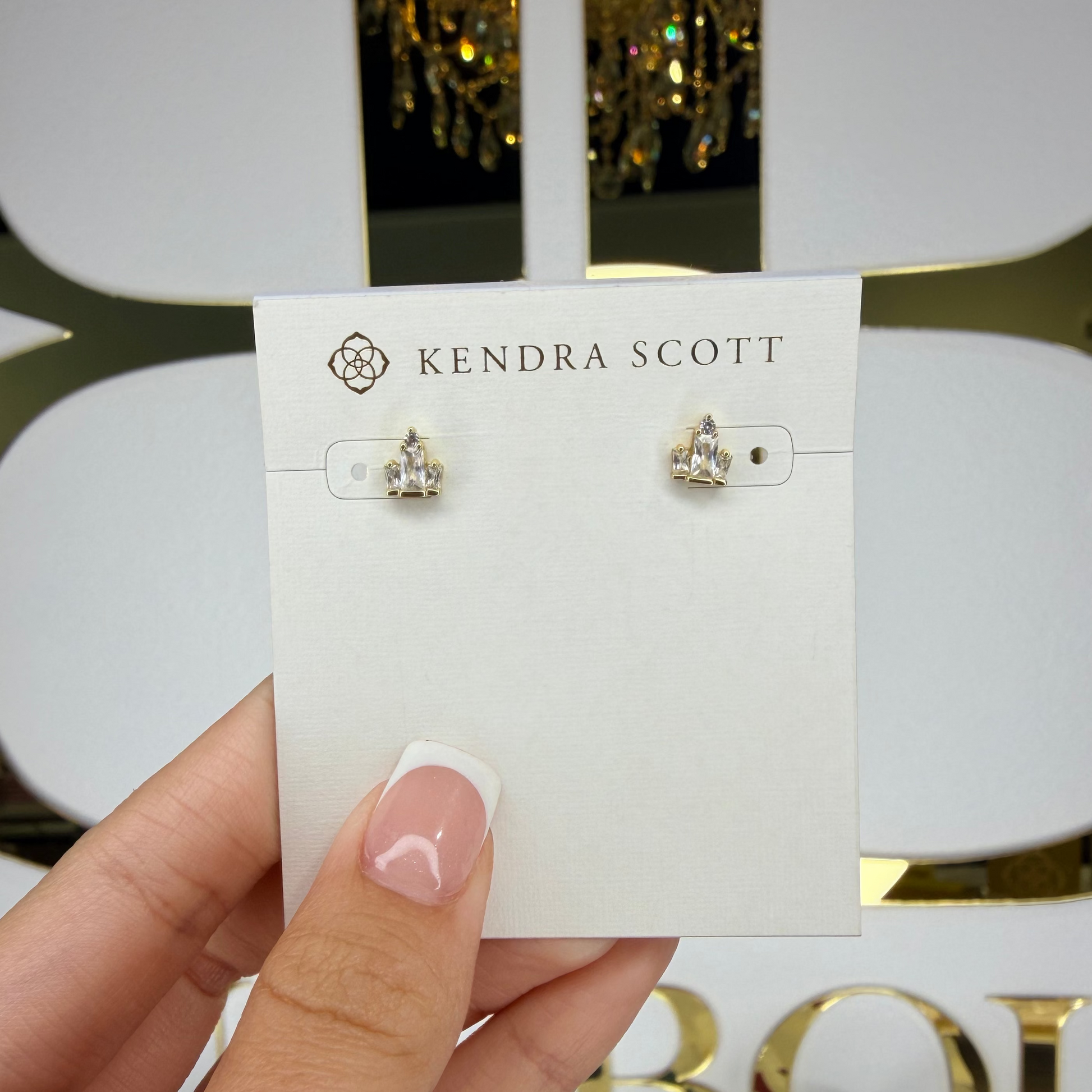 Kendra Scott earrings on a card held by a hand with a blurred background