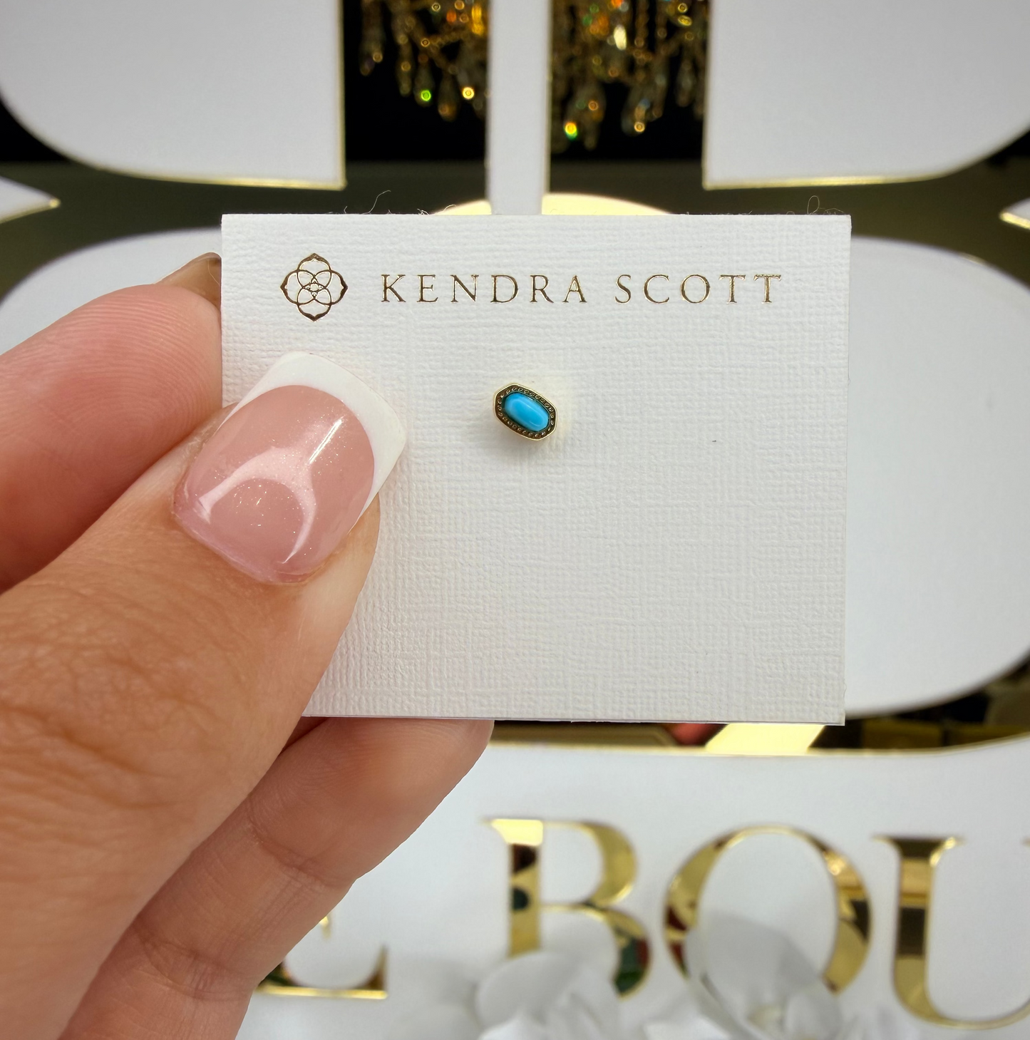 Kendra Scott earring on a display card held by a hand with a blurred background