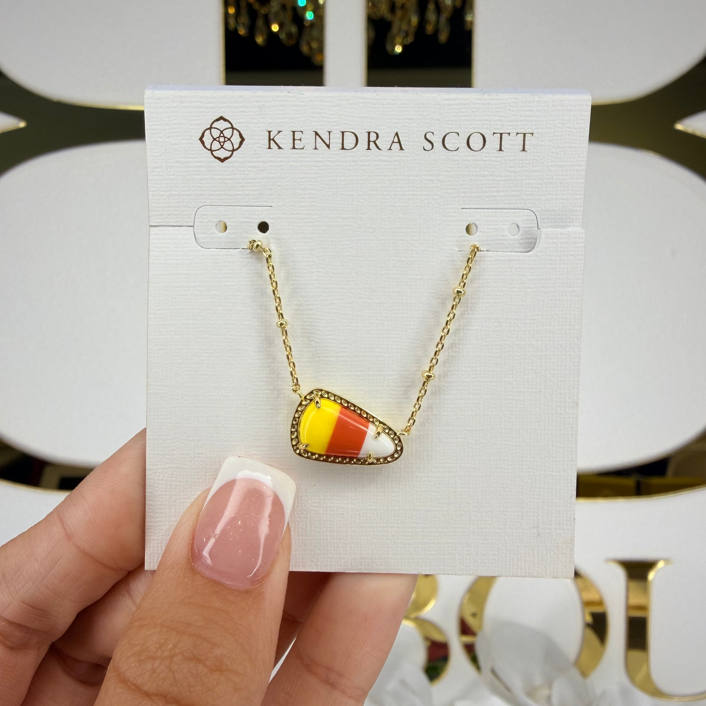 Kendra Scott necklace on a card held by a hand with a decorative background