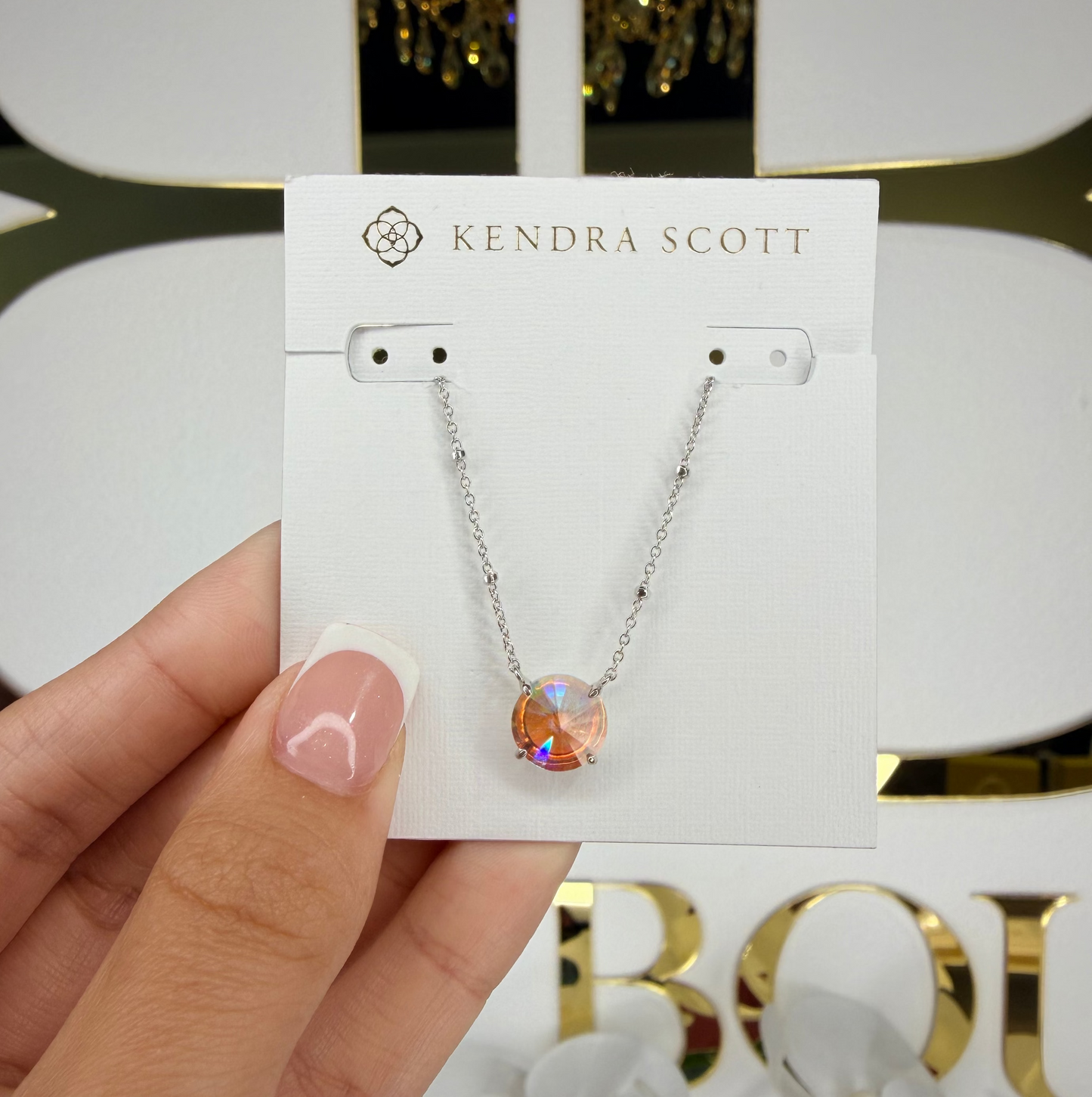 Kendra Scott necklace on a card held by a hand with a blurred background