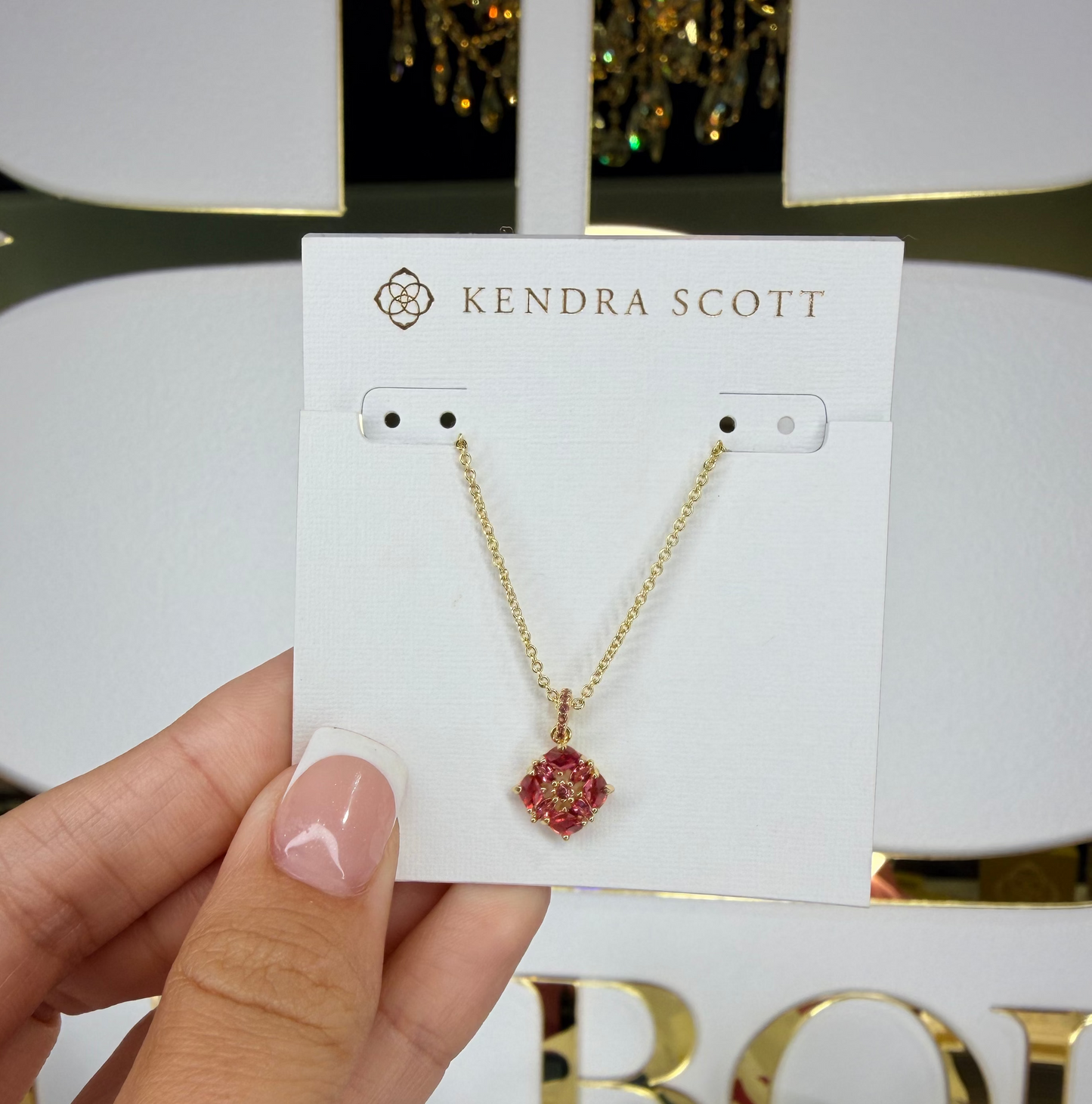 Gold necklace with a red flower pendant on a Kendra Scott card, held by a hand.