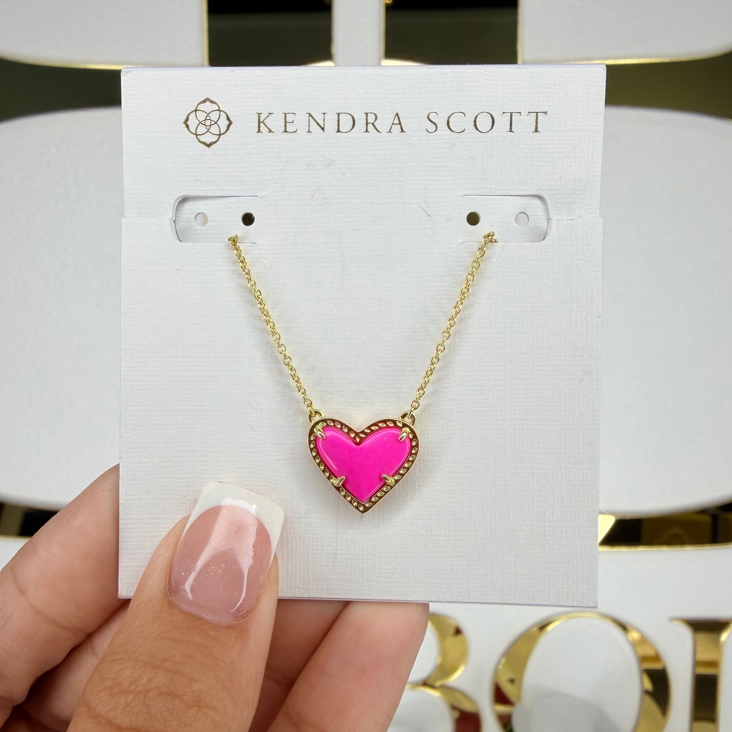 Heart-shaped pink pendant necklace on a Kendra Scott card held by a hand.