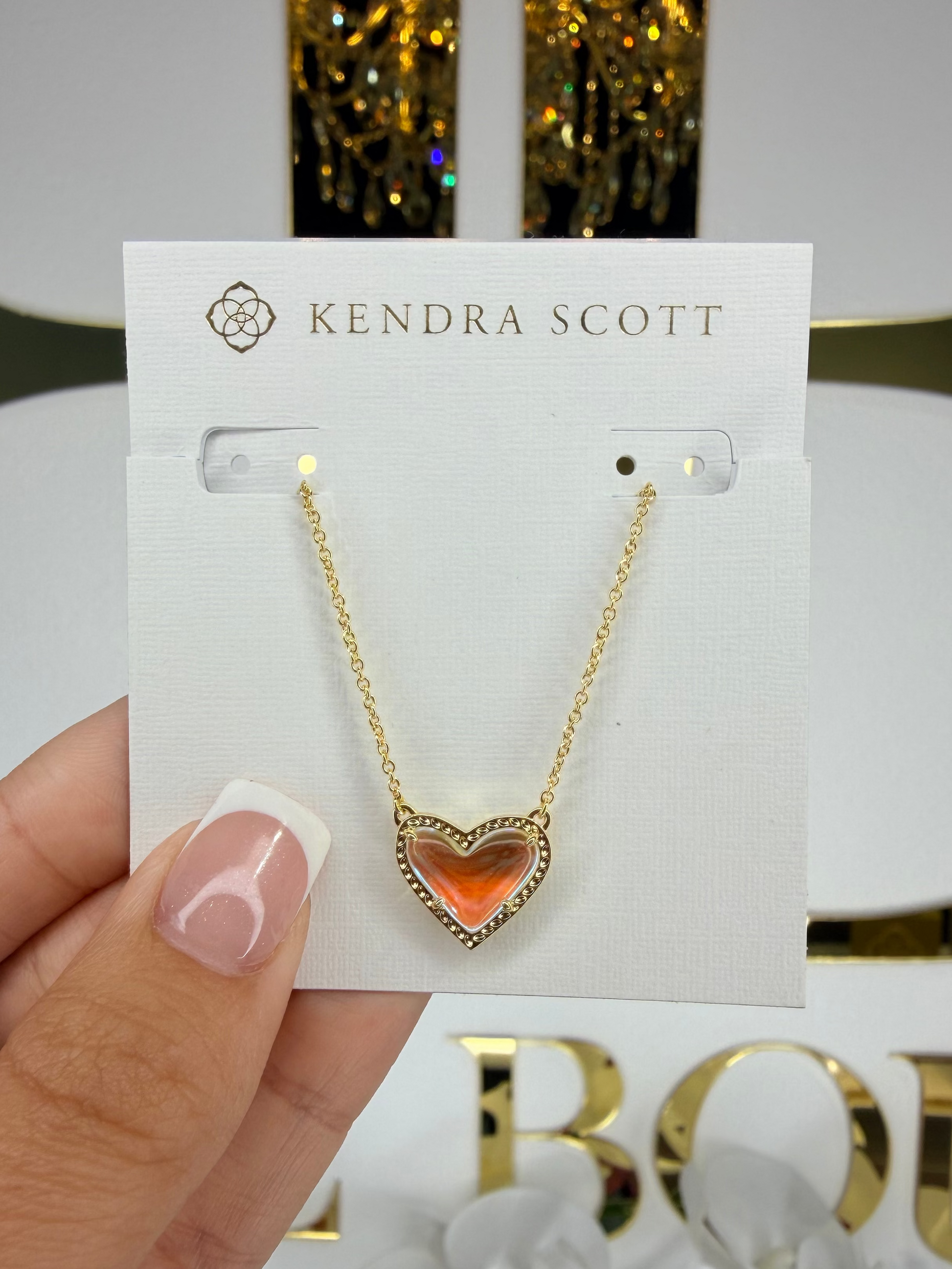 Kendra Scott necklace with heart-shaped orange pendant held on a card