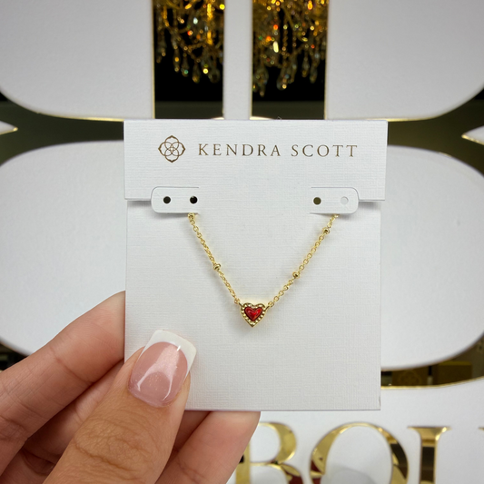 Gold necklace with a red heart pendant on a Kendra Scott card, held by a hand.