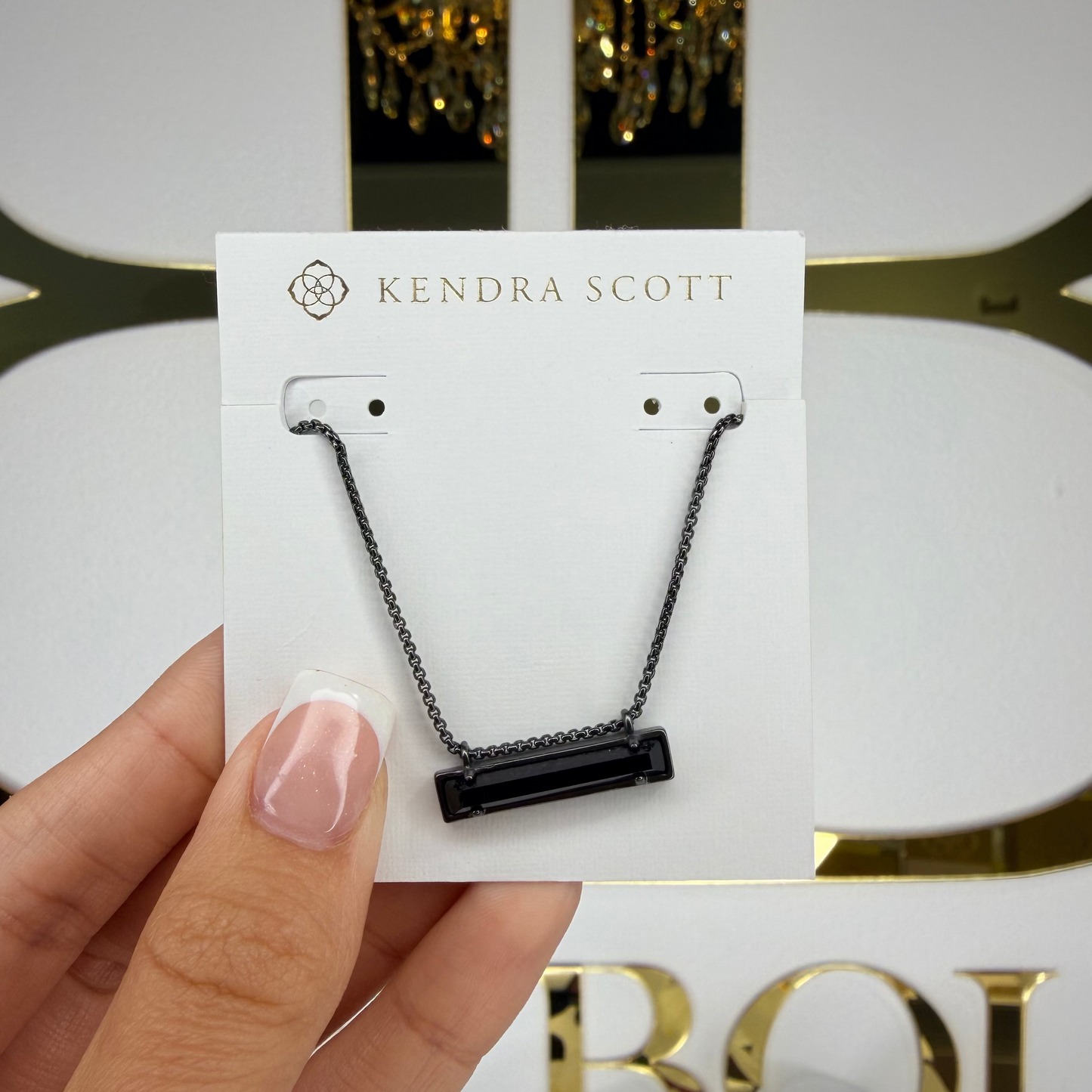 Kendra Scott necklace on a card held by a hand with a decorative background