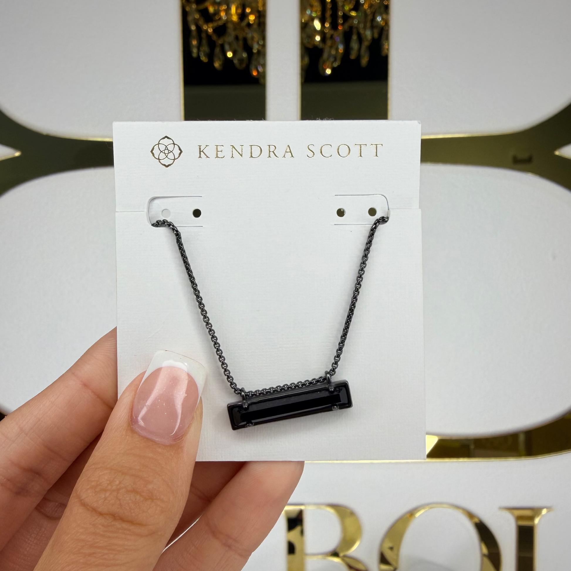 Kendra Scott necklace on a card held by a hand with a decorative background