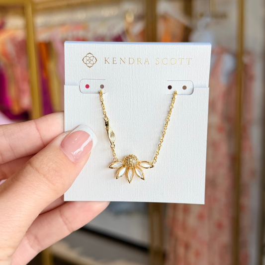 Gold necklace on a Kendra Scott card held by a hand with a blurred store background