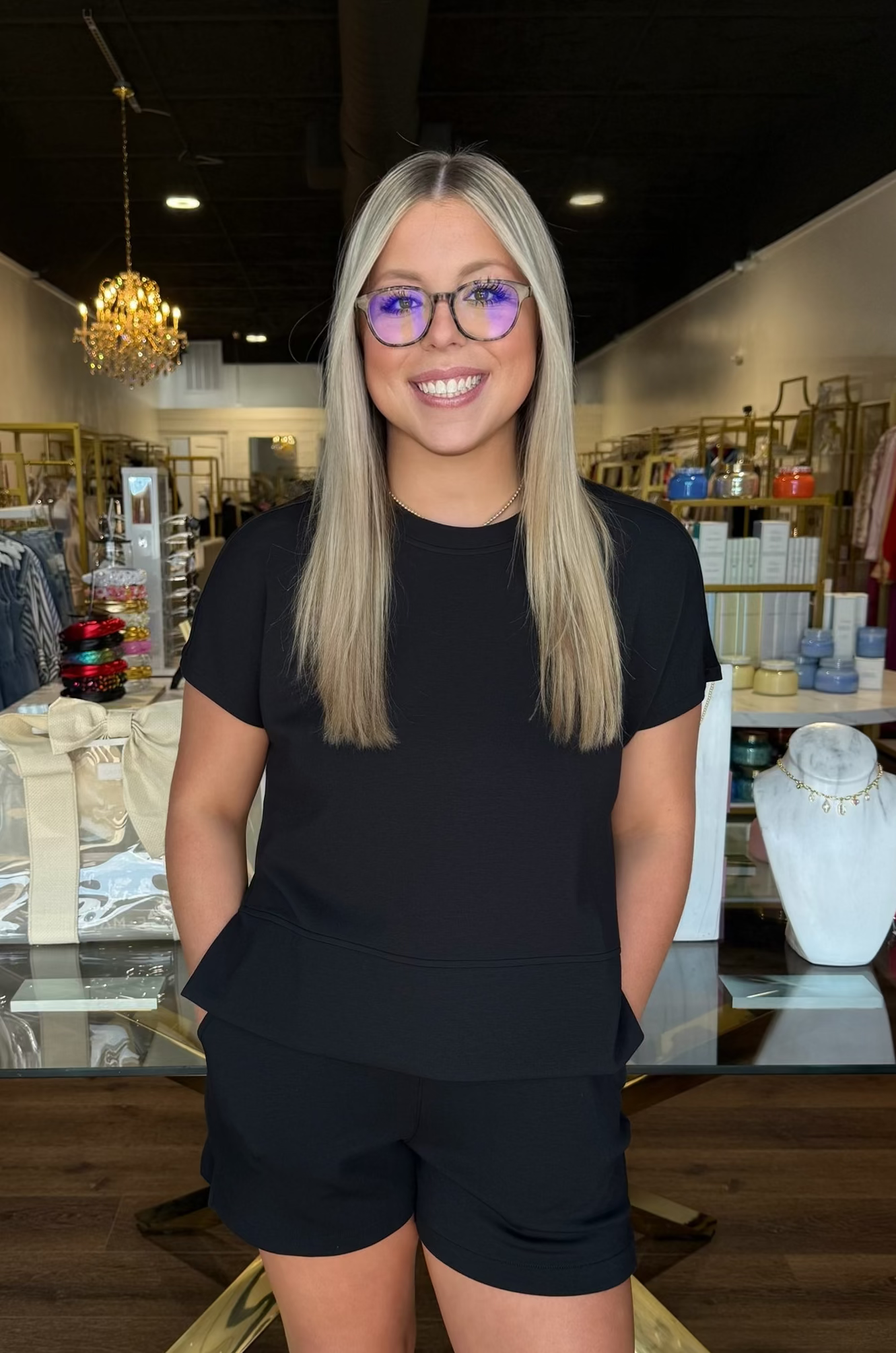 Woman in a black t-shirt and shorts standing in a store with various items on shelves and tables.