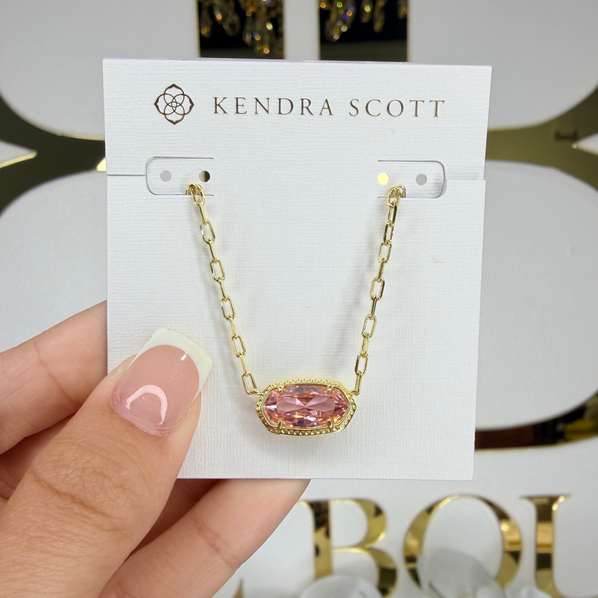 Kendra Scott necklace on a card held by a hand with a blurred background