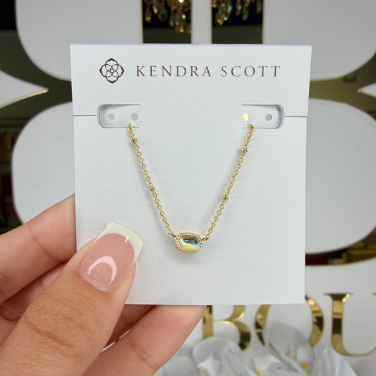 Gold necklace on a Kendra Scott card held by a hand with a decorative background