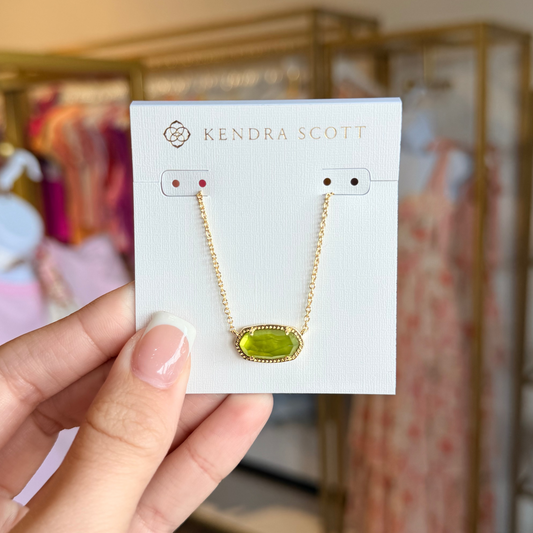 Kendra Scott necklace on a card held by a hand with a blurred store background