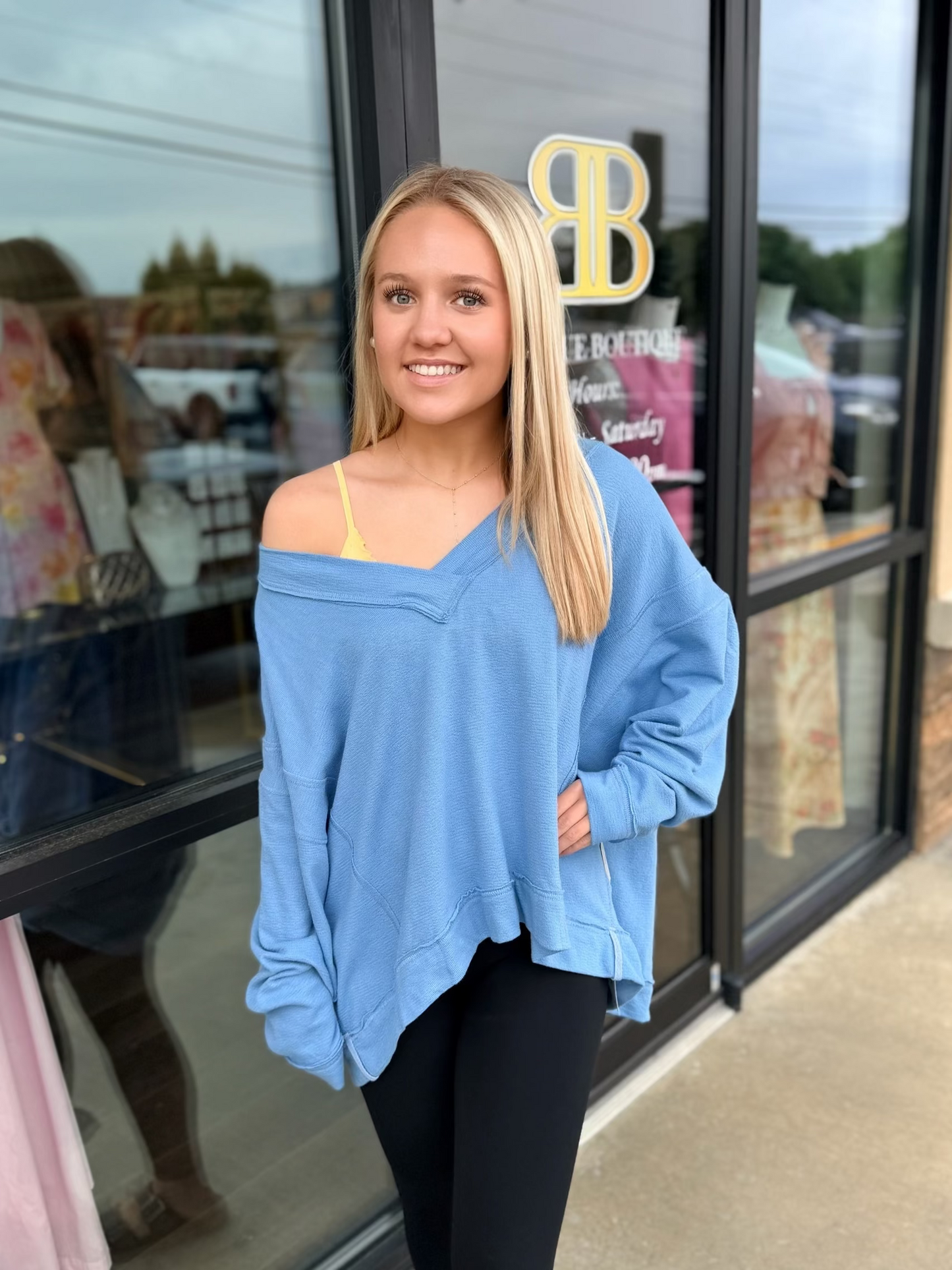Woman in a blue sweater standing outside a store with a large 'BB' sign.
