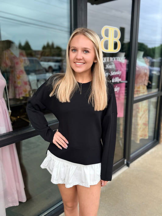 Woman wearing a black sweater and white skirt standing in front of a store window.