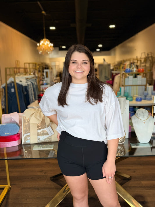 Model standing infront of store with white shirt and black biker shorts 