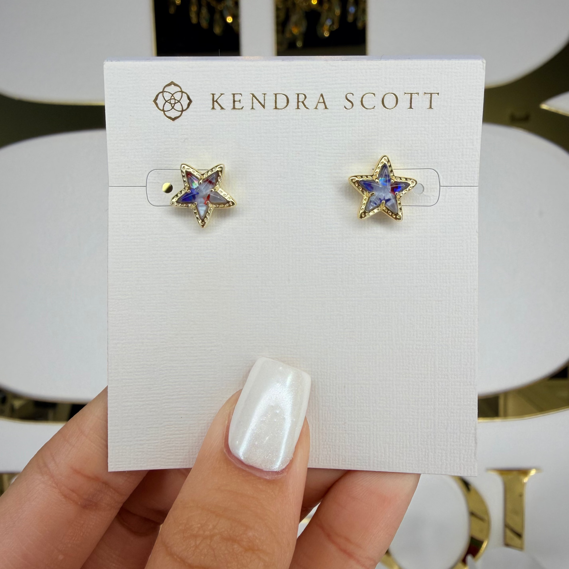 Star-shaped earrings on a Kendra Scott card held by a hand with white nail polish.