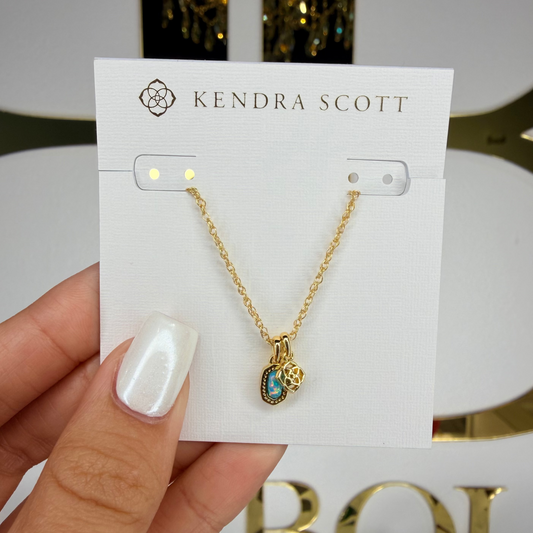 Gold necklace on a Kendra Scott card held by a hand with white nail polish.