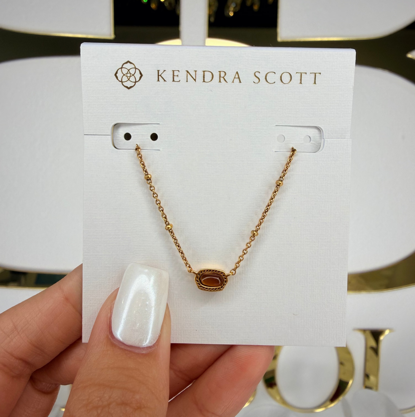 Kendra Scott necklace on a display card held by a hand with a blurred background
