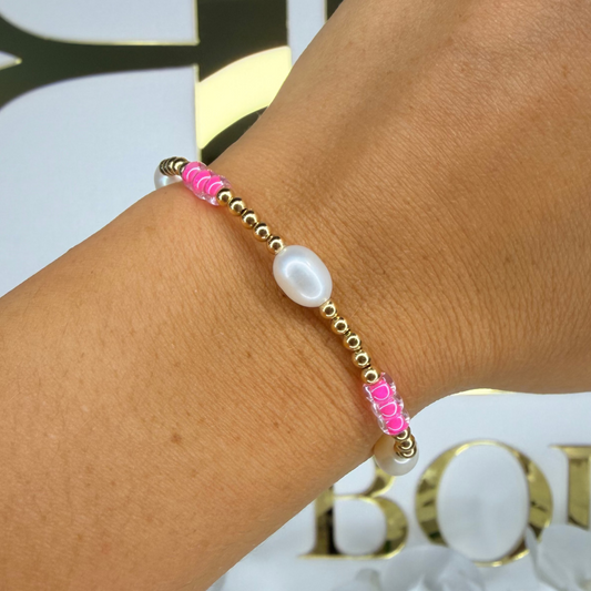 Bracelet with pink beads and a pearl on a wrist, with a blurred background