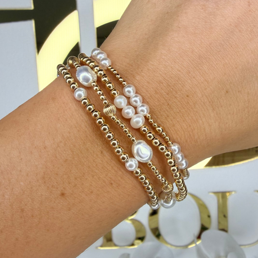 Close-up of a wrist wearing multiple pearl and chain bracelets with a blurred background.
