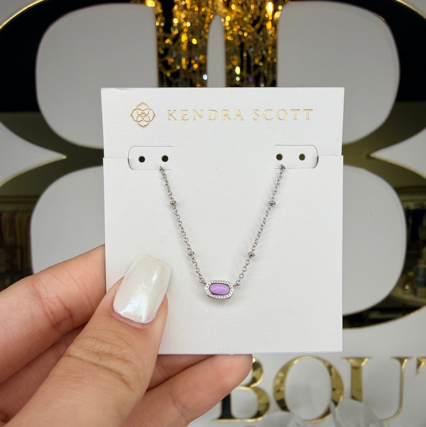 Kendra Scott necklace on a card held by a hand with a decorative background