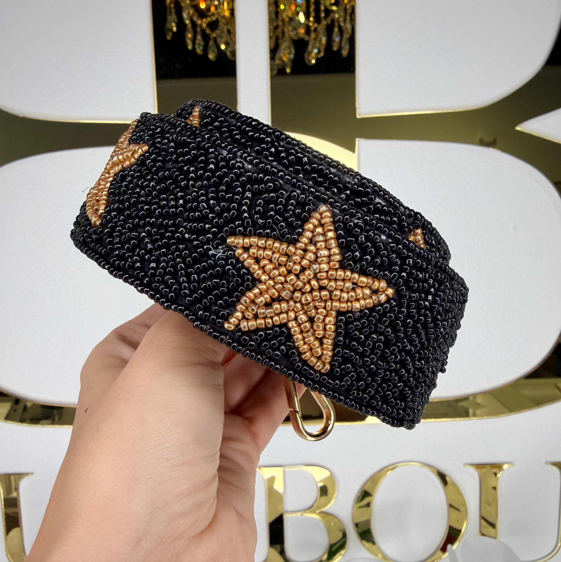 Black beaded headband with gold stars held by a hand against a decorative background.