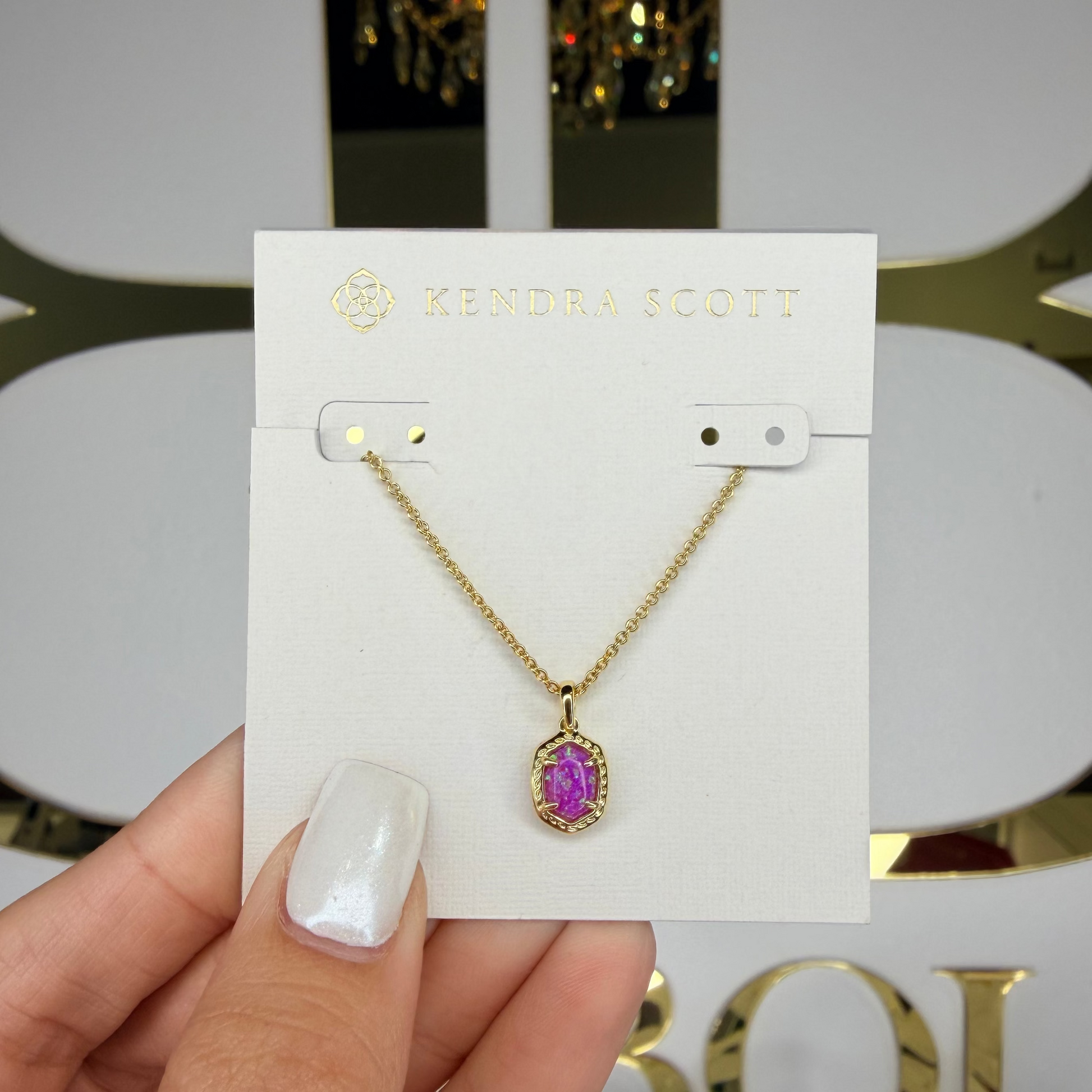 Gold necklace with a purple pendant held on Kendra Scott card
