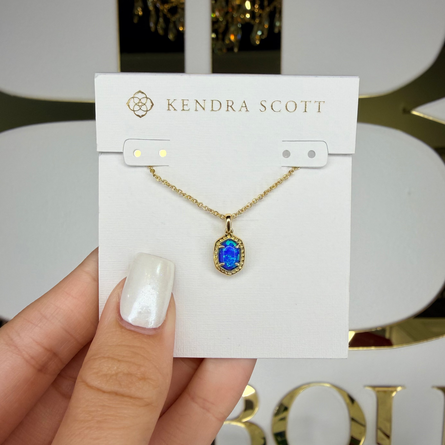 Kendra Scott necklace with blue pendant held on a branded card