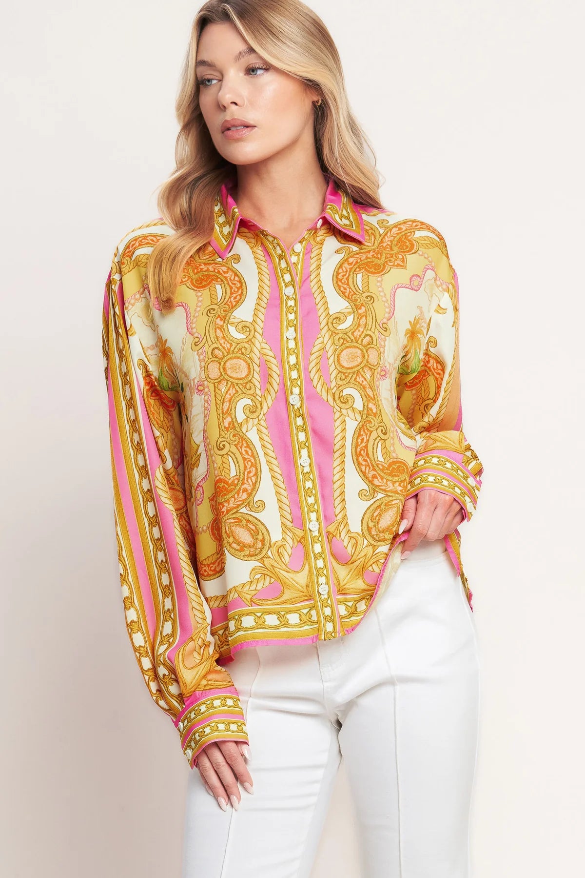 Woman wearing a colorful patterned blouse with white pants on a plain background