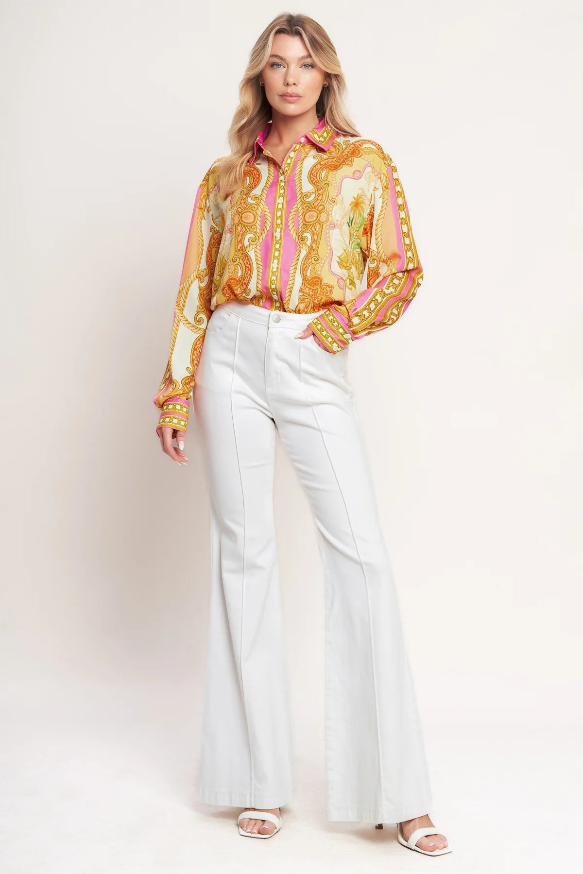 Woman wearing a colorful patterned blouse and white pants on a plain background