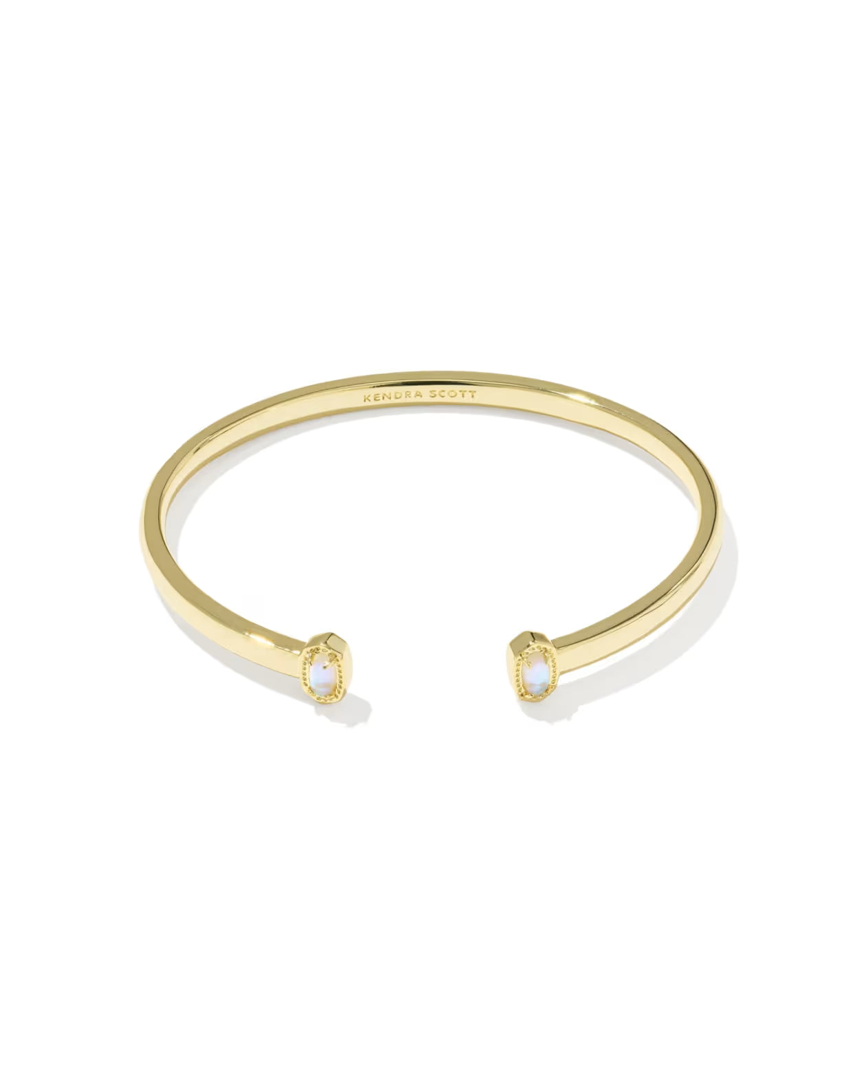 A gold open cuff bracelet by Sandra Scott, featuring two small oval bezel-set white stones at the ends, shown on a clean white background.