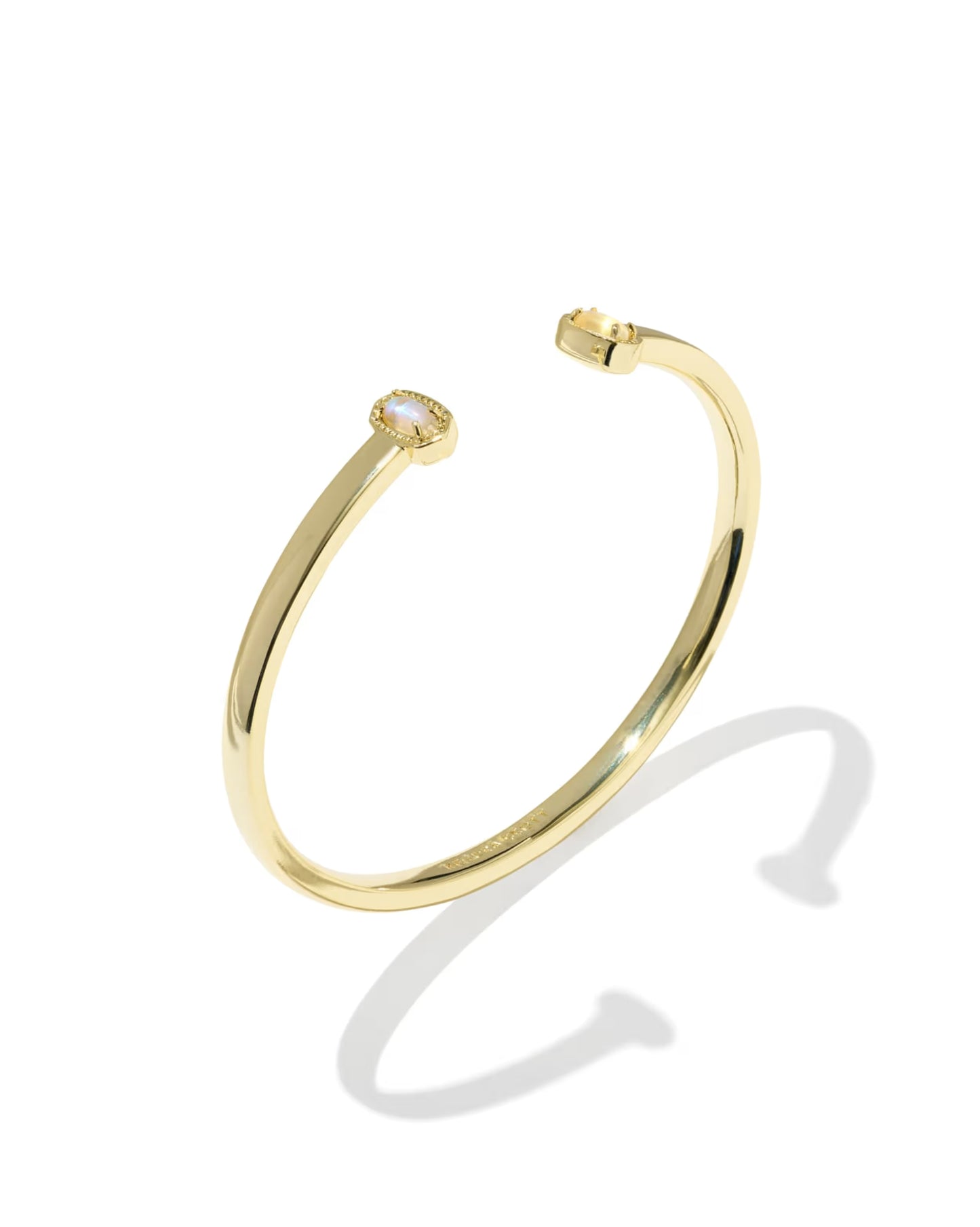 A polished yellow gold open cuff bracelet with a small bezel-set white gemstone on one end, shown on a clean white background with a soft shadow.