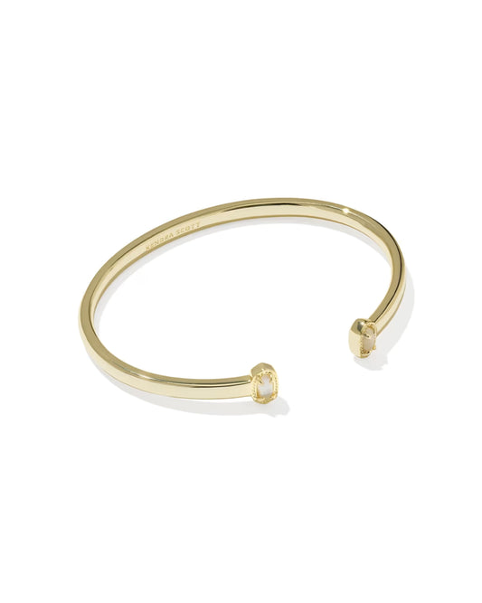 A slim gold-tone open cuff bangle bracelet with a small clear gemstone set at each end, shown on a clean white background.