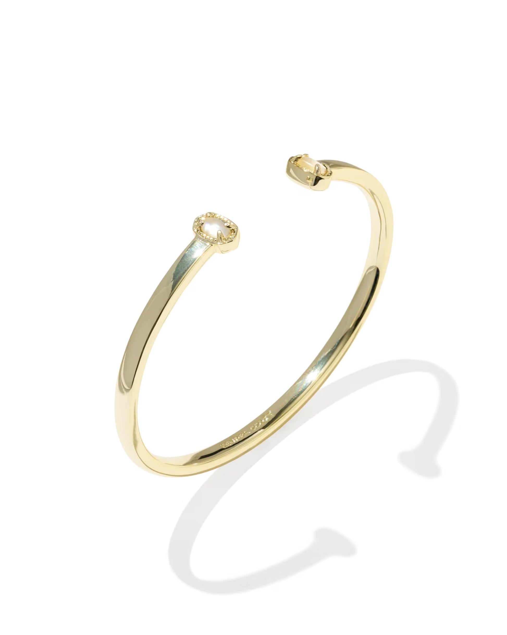 A polished yellow gold open cuff bangle bracelet with a small halo-style diamond setting on one end, shown on a clean white background with a soft shadow.