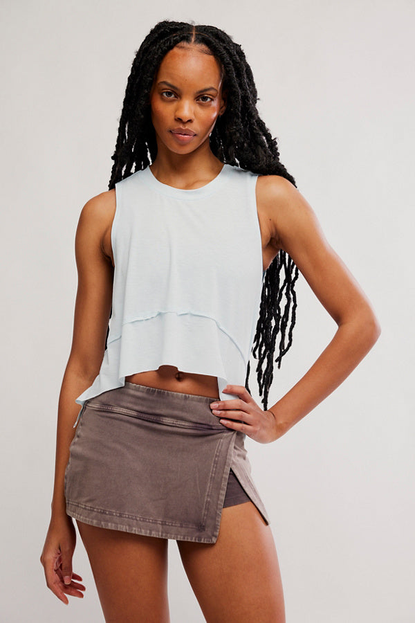 Woman wearing a light blue sleeveless top and brown denim skirt on a plain background