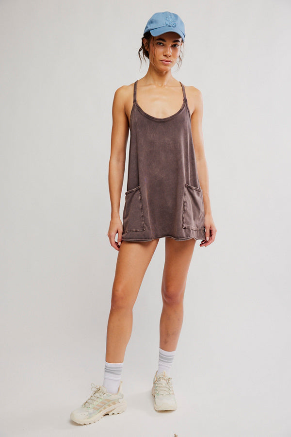 Person wearing a brown slip dress, blue cap, and white sneakers on a plain background