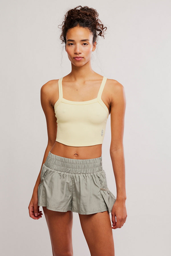 Woman wearing a yellow tank top and light gray shorts on a plain background