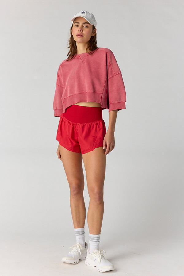 Person wearing a pink sweatshirt and red shorts on a white background
